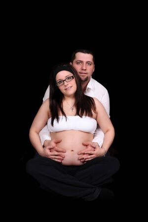 Happy expectant couple sitting holding bare belly. isolatedの写真素材