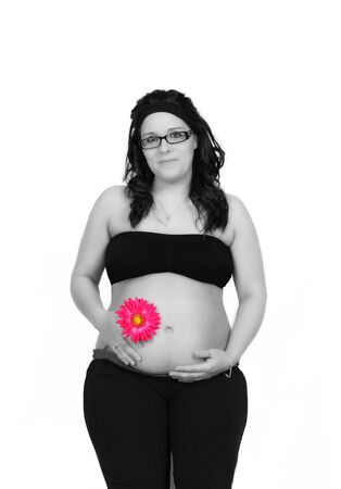 beautiful pregnant smiling woman in black and white standing with bare belly and vibrant pink daisy flower in hand in full colour. isolated on whiteの写真素材