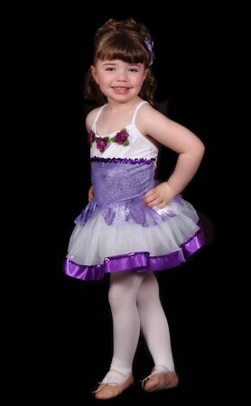 adorable little girl in purple and white ballet costume standing and posing proudly. isolated on blackの写真素材