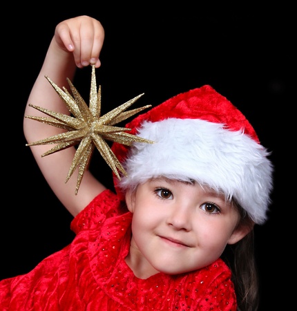 adorable girl in Christmas outfit playing with golden star ornament. isolated on blackの写真素材