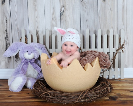 adorable baby sitting in giant easter egg with hat and bunnyの写真素材