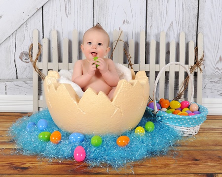 adorable baby boy sitting in giant easter egg surrounded by colourful Easter grass and eggsの写真素材