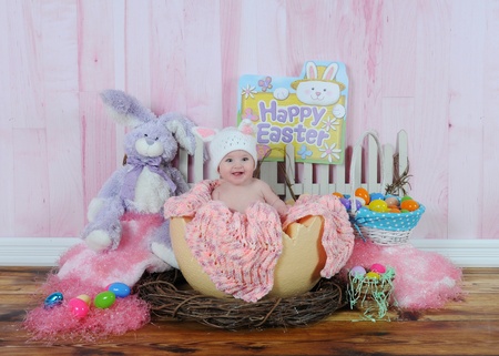 happy baby girl sitting in easter egg surrounded by easter decorationsの写真素材