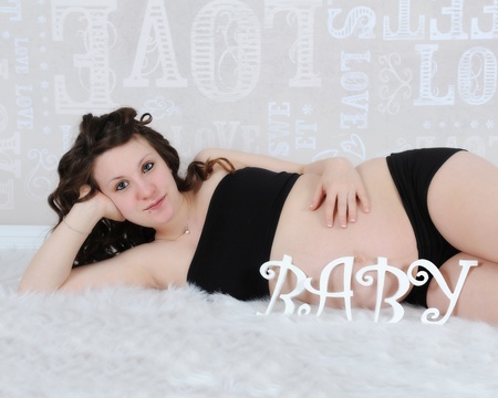 beautiful pregnant woman laying with the word baby spelled out in front of her bellyの写真素材