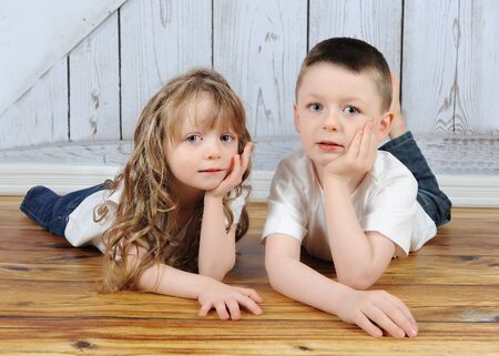 young brother and sister laying together in floor with hands on chinの写真素材