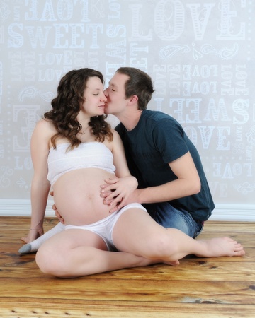 man lovingly kissing expectant womans cheek with his hands on her belyの写真素材