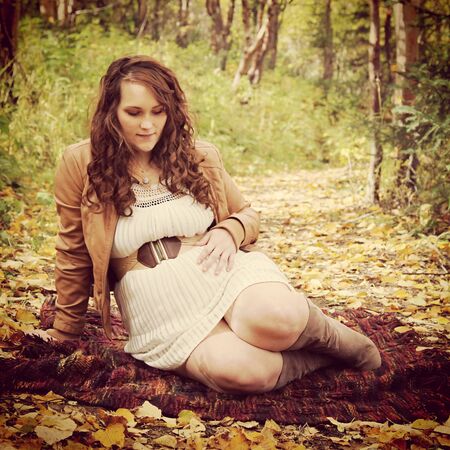 beautiful of pregnant woman sitting on forest path in fallの写真素材