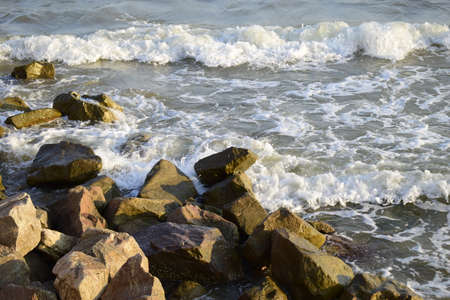 Sea surf, the blue wave hits the rocks. Coastline foam from breaking on the rocks of the sea surf. Wet stones and waves. Background of sea stones and the sea serf for design.の写真素材