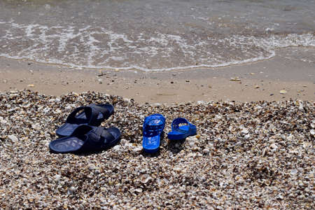 Summer slippers on the beach near the water. Sea shells on a sunny day. Tropical beach vacation and travel conceptの写真素材