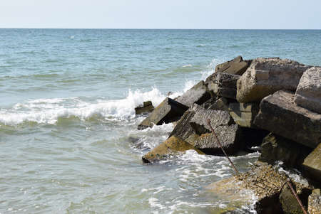 The waves of the turquoise sea break on the coastal boulders and a dense white foam is formed. clear...