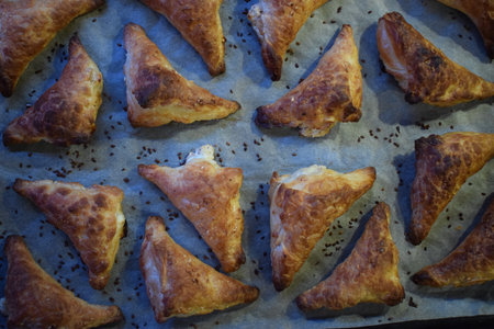A baking tray filled with freshly baked golden brown triangular cakes. The cakes have a flaky, crunchy texture, are sprinkled with sesame seeds on top. They spread evenly on a sheet of parchment paperの写真素材