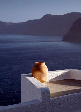 Sunlit Greek Urn in Oia town on the Greek Island of Santorini with blue sea and mountains in backgroundの写真素材