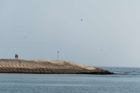 couple walking breakwater built concrete blocks pier to ocean salalah omanの写真素材