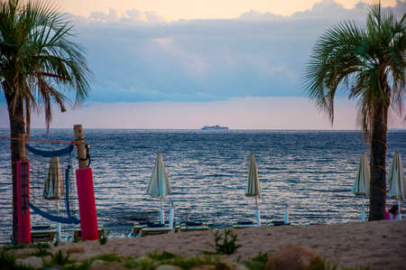 Beautiful sunset landscape with cruising boat on ocean tropical beach with palms sardegna italy
