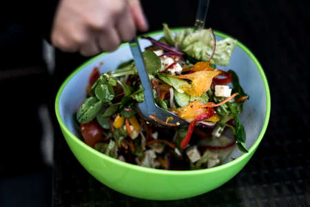 Delicious fresh healthy salad in a green bowl mixed by a woman hands with salad spoon foodの写真素材