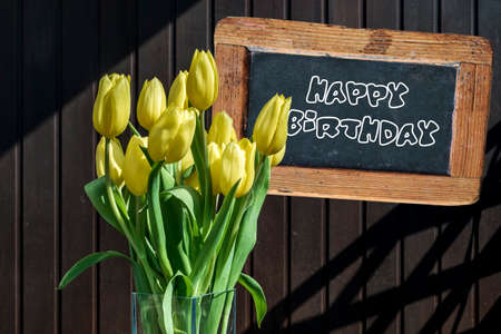 Wooden chalkboard happy birthday Sign beautiful yellow tulips bucket spring flowers tulip brown backgroundの写真素材