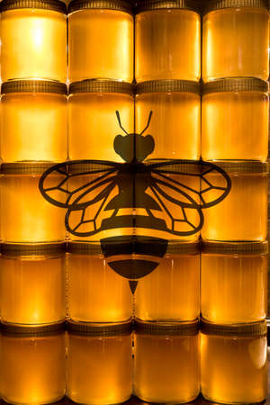 Golden yellow honey in glass jar on wooden board. Closeup. Copy space. with bee logoの写真素材