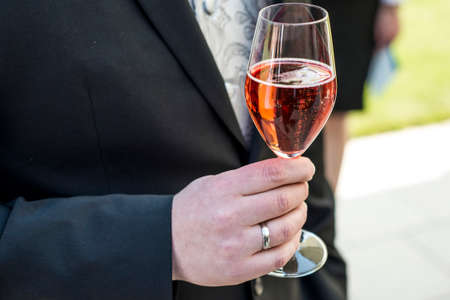 Groom holding glass sparkling wine wedding red champagne in suit closeup ring fingerの写真素材