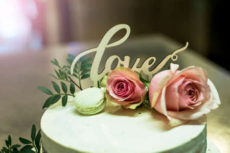 Beautiful wedding cake with cream With text Love on top and pink flowers rosesの写真素材