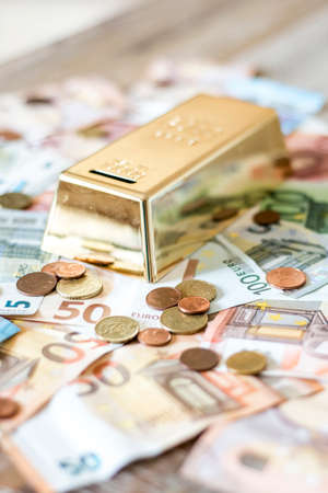 savings Cash money concept euro banknotes of all sizes and cent coins on desk piggy bank gold bar shape saveの写真素材
