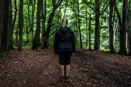 Beautiful woman hiker standing on forest trail looking away. Female on hike in nature spooky mystical forestsの写真素材