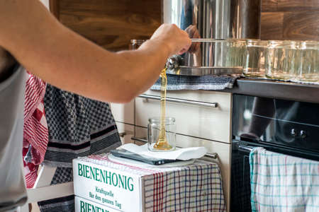 Beekeeper filling up fresh golden honey into glass jar white cardboard boxes saying german Beehoney...