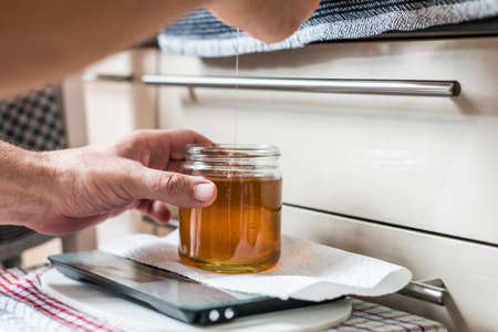 Beekeeper filling up the fresh golden new honey into glass jars on a scale scalesの写真素材