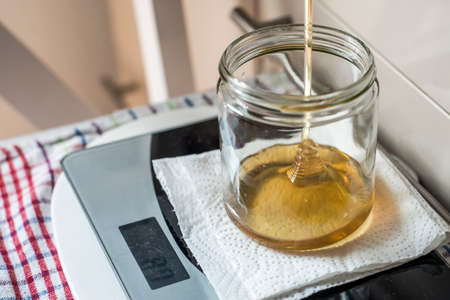Beekeeper filling up the fresh golden new honey into glass jars on a scale scalesの写真素材
