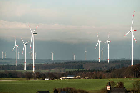Village in front of panorama view over wind farm landscape in Germany with white generator turbines