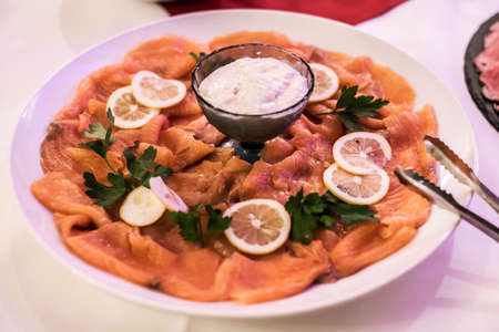 Raw salmon with lemon slices herbs and dip on white plate at dinner buffet lunchの写真素材