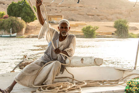 ASWAN, EGYPT 21.05.2018 Old Nubian Man Sitting on Felucca Boat Deck and Sailing Down the Nile Riverのeditorial素材