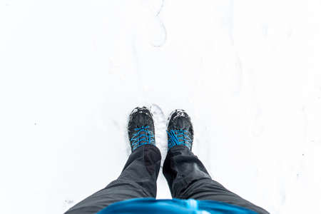 First person view of legs in hiking boots in the snow. Snow on boots while walking in winter