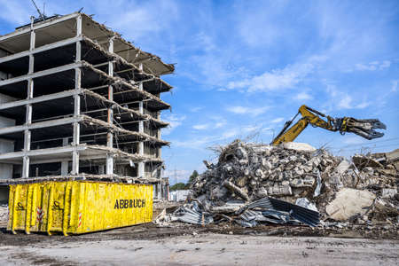 Building Demolition site Excavator hydraulic crasher and yellow container written word abbruch is...