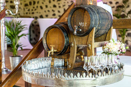 Old oak barrel with whiskey spirit small glases on a wooden table. in front of blurred background...