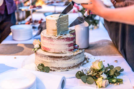 cutting a beautiful delicious Wedding cake in many tiers with fresh wild flowers and roses