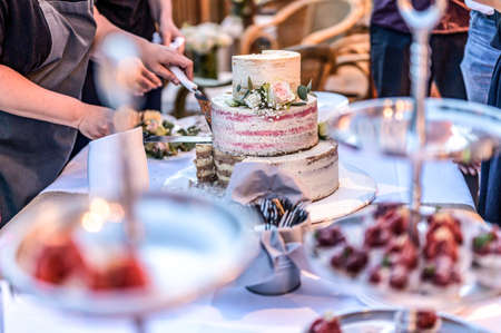 cutting a beautiful delicious Wedding cake in many tiers with fresh wild flowers and rosesの写真素材
