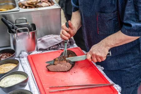 Chef cut with a Knife a smoker smoked Meat Steak filet on a red cutting board grilling bbq southfood themeの写真素材