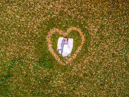 Aerial view of marriage couple lying in a shape of heart made of fall Autumn leafes woods drone photo romantic loveの写真素材