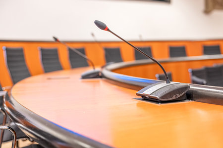 Microphones and round brown table in an empty conference room. Beginning of session meeting with...