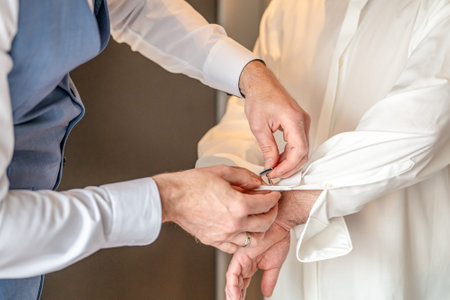 Man groom tying cufflinks on shirt sleeves getting dressed with closeup of hands no face