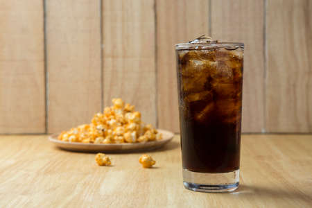Refreshing Cola with Ice and Popcorn on a wooden background