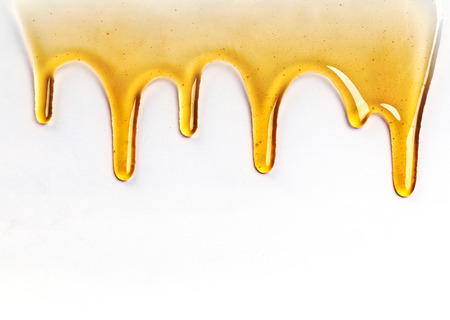 Dripping golden sweet honey flowing down the frame from the top over white with copyspace and textの写真素材