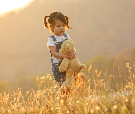 Sad little girl feeling alone in the park concept. Lonely beautiful toddler girl stay alone in the park. at sunset with flareの写真素材
