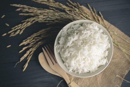 Cooked rice with dry rice and ears of jasmine rice on wooden tableの写真素材