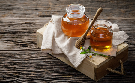 Honey bee in jar with honey dipper and flower on wooden table, bee products by organic natural ingredients concept, copy space for your textの写真素材