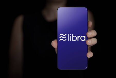 Close up of young woman hand holding Smartphone with Libra logo isolate on black backgroundの写真素材