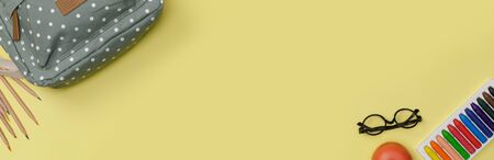 Creative flatlay of education yellow table with backpack, student books, colorful crayon, eye glasses, empty space in studio shot isolated on yellow long banner background, Concept of education and back to schoolの写真素材