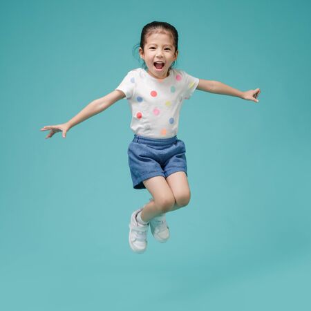 Playful energetic Asian little girl jumping in mid-air, empty space in studio shot isolated on...