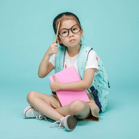 Cute child with book thinking and learning, studio shot isolated on colorful blue background,...