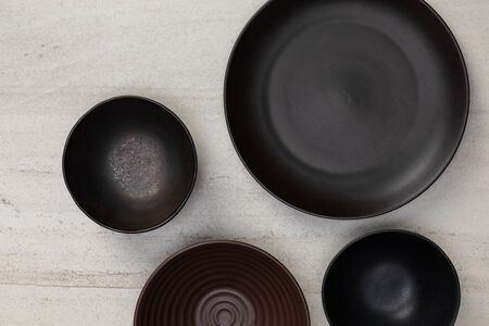 Group of empty blank black ceramic round bowls and plates on white stone blackground, Top view of...